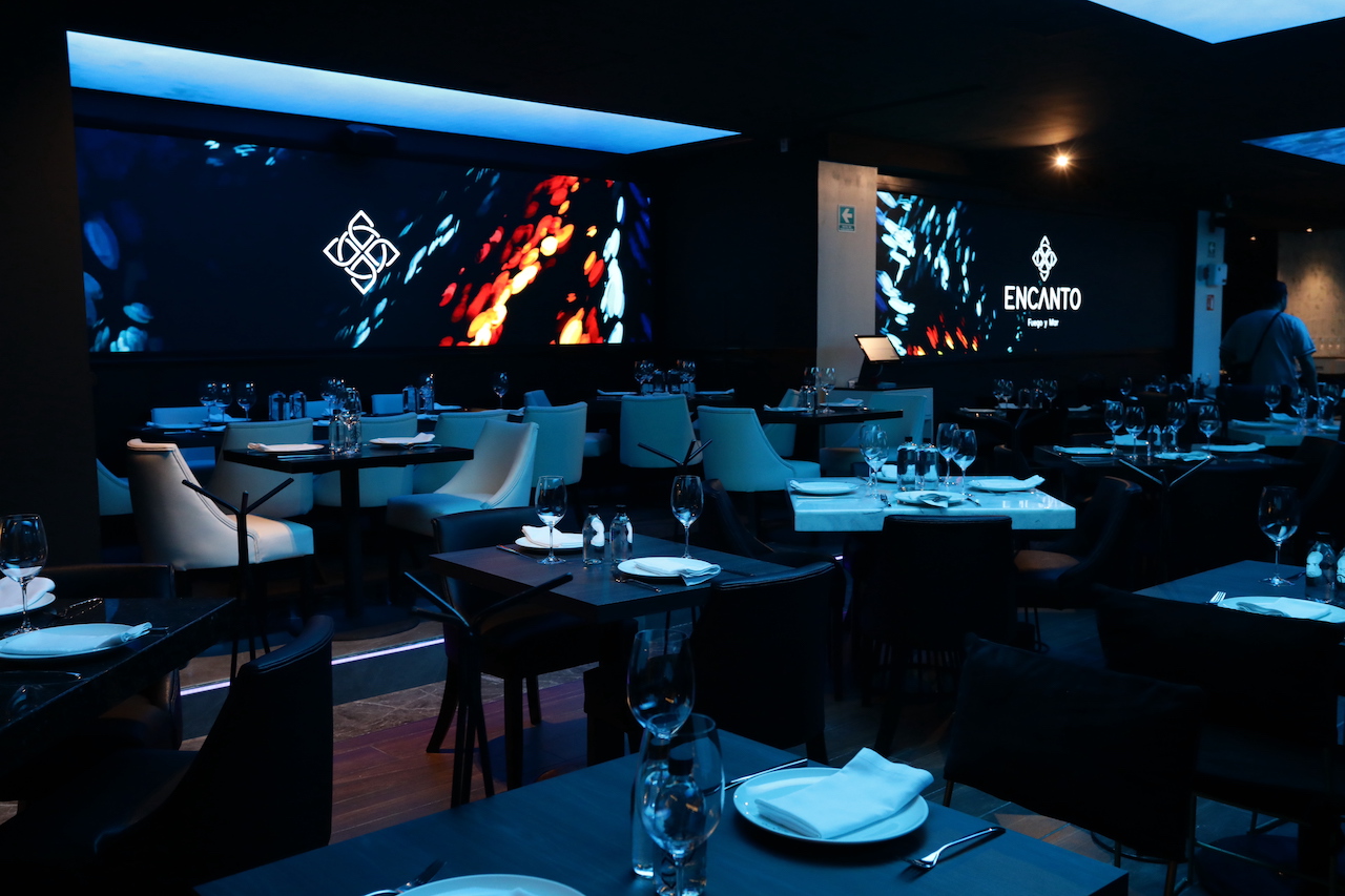 Restaurante Encanto Fuego & mar por dentro, se aprecian pantallas monumentales proyectando imágenes inversivas al rededor de la mesa