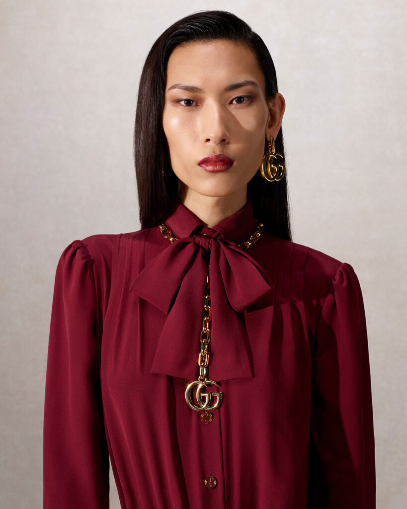 Modelo con blusa en color borgoña y collar con el logo de la marca