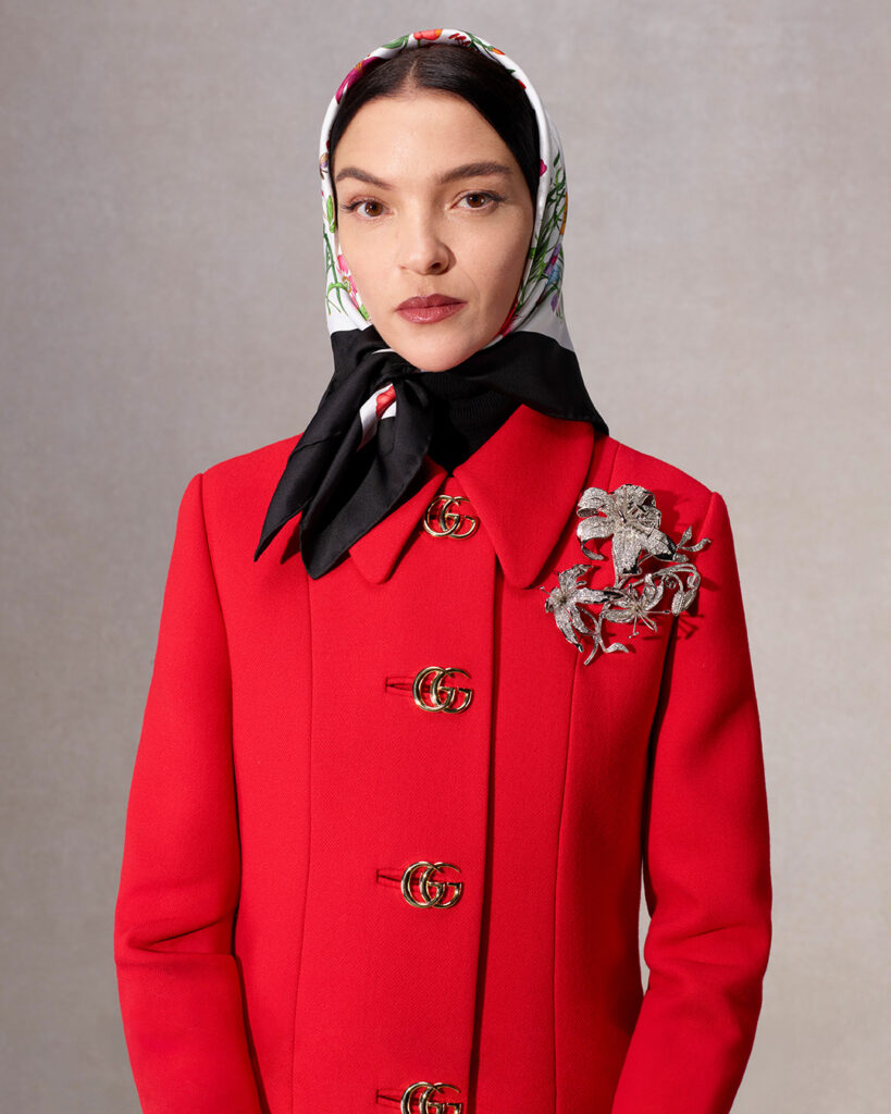 Modelo con zaco rojo con botones del logo de la marca y mascada en la cabeza 