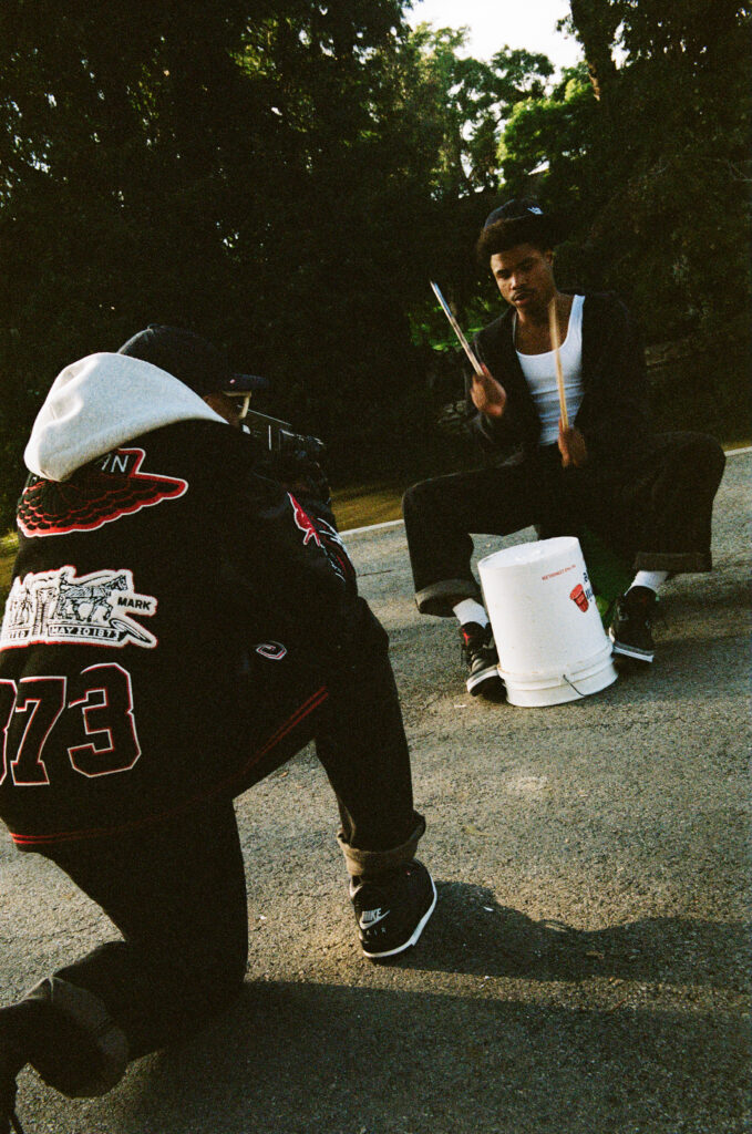 chico con dos palos de bateria una cubeta y chamarra