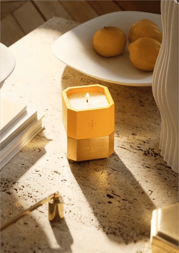 Vela en color amarillo con dorado sobre una mesa de mármol al lado de un plato con limón amarillo 