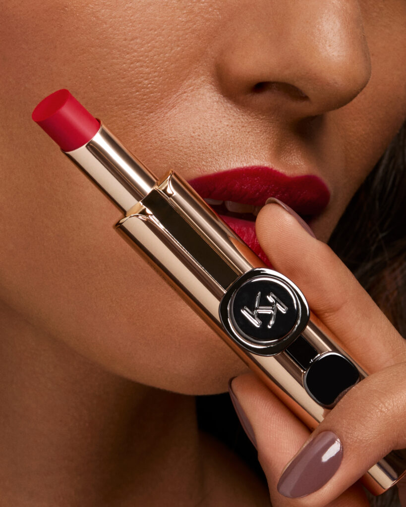 Labial rojo con empaque dorado y de fondo rostro de modelo con el labial rojo