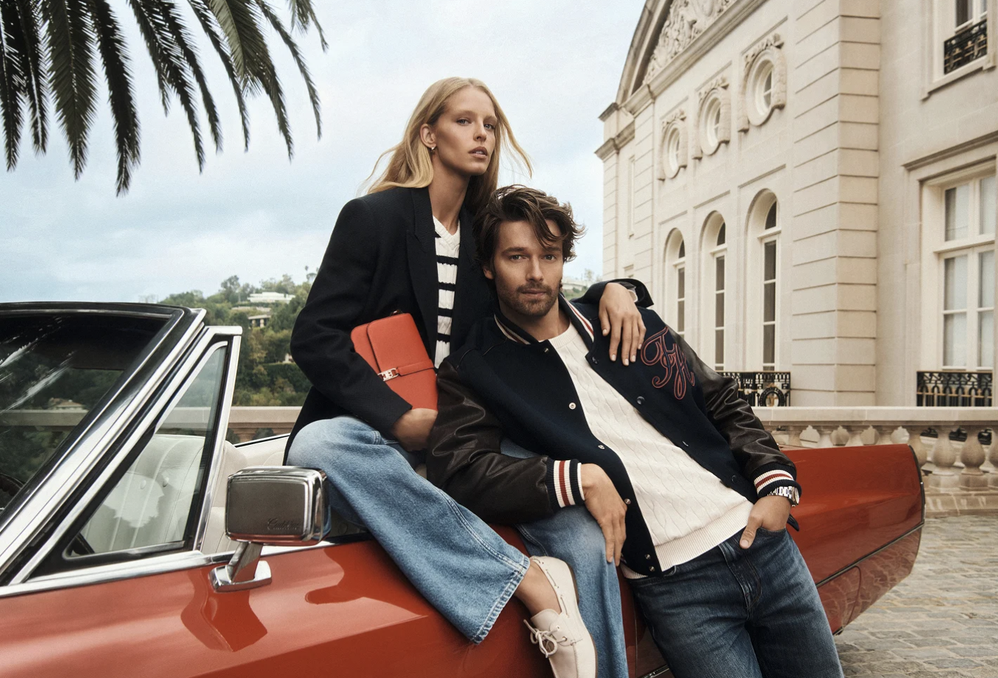 hombre y mujer vestidos con ropa de Tommy hilfiger recargados en un coche clasico rojo