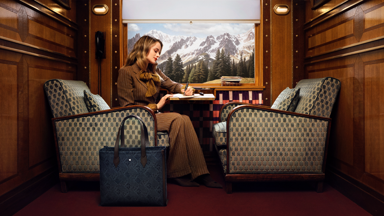 Joey King sentada en un sillón a un lado del sillón un bolso Montblanc