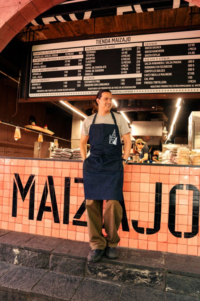 retrato de chef Santiago Moctezuma, de Maizajo posando en la entrada de la tienda y de fondo la cocina
